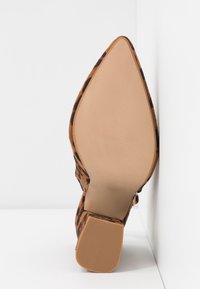 Chaussure à talon haut en daim à imprimé léopard, avec un bout pointu. Dispose d'une semelle en caoutchouc lisse couleur beige et d'un talon assorti.