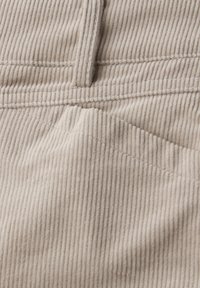 Tissu en velours côtelé beige avec des côtes verticales visibles et des coutures détaillées autour d'une poche et d'une couture.