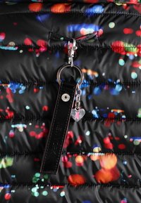 Doudoune noire avec un motif coloré de pois. Comprend un porte-clés brillant avec une sangle noire et un charm en forme de cœur.