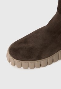 Ruda suvaira batai su storu beige briaunuota guma sola, pateikti artimu planu iš šono ant vienodo fono.