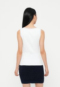 Top alb fără mâneci, cu guler rotund și textură netedă, asortat cu o fustă mini tricotată texturată de culoare bleumarin, văzut din spate.