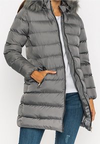 Šedý prošívaný kabát s kapucí lemovanou umělým kožíškem, zapínáním na zip a bočními kapsami. Vyznačuje se prošívaným vzorem a lehkou texturou.