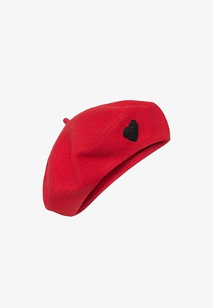 Czerwona wełniana beret z małym czarnym haftem serca z boku oraz z cienkim szpulowym elementem na górze, na białym tle.