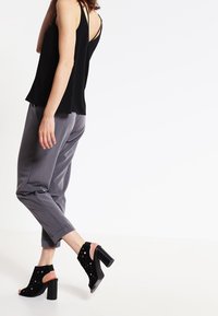 Svart ärmlös topp med en lös passform och korslagd baksida, matchad med grå smala byxor. Svarta öppen-toe blockklack sandaler med utskärningar.