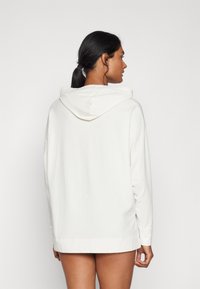 Vit hoodie i avslappnad passform, med långa ärmar och dragsko i huvan. Mjuk textur och nederkant som faller strax under höfterna.