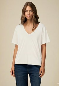 Tricou alb cu decolteu în V și mâneci scurte, fabricat dintr-un material moale. Purtați-l cu blugi denim albaștri, având o croială lejeră și o textură netedă.