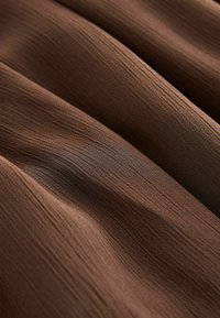 Tissu marron avec de fines plis verticaux et des plis doux créant une surface texturée et ondulée.