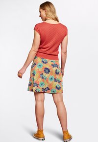 Rdzawoczerwony, krótki top z wzorem serca; połączony z spódnicą w kwiatowy wzór, z zielonymi i niebieskimi kwiatami na pomarańczowym tle.