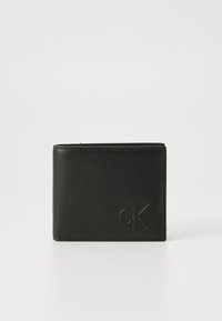 Černá kožená peněženka s hladkým povrchem. Na přední straně se nachází embosované logo "cK". Kompaktní obdélníkový tvar s zaoblenými okraji.