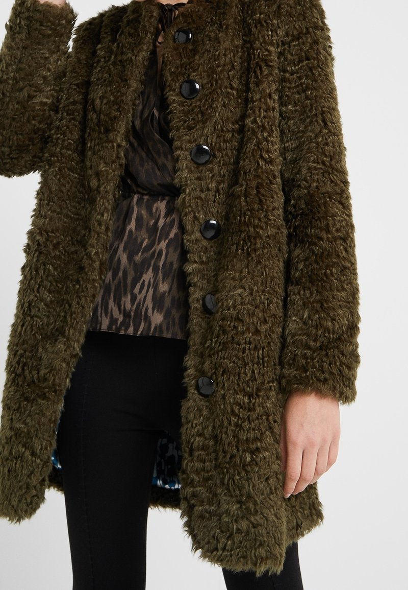 Olivgrüner Kunstpelzmantel mit strukturiertem, flauschigem Material. Verfügt über schwarze Knöpfe und eine leicht übergroße Passform. Innenfutter mit blauem Muster.