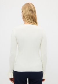 Weißes, geripptes Langarmshirt mit taillierter Passform und Perlenakzenten an den Manschetten. Weicher Stoff und klassischer Rundhalsausschnitt.