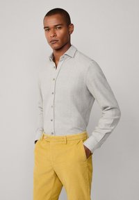 Camisa de botón gris claro de manga larga, con un cuello clásico y una textura sutil, combinada con pantalones de pana amarillos.