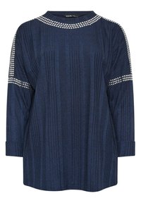 Marinblå, långärmad topp med ribbad struktur, dekorerad med silverfärgade nitar längs axlarna och halsringningen. Mjuk tygkvalitet, avslappnad passform.