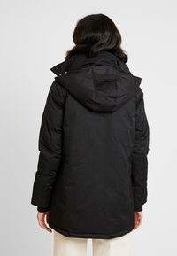 Cappotto invernale nero con cappuccio, caratterizzato da una texture liscia, polsini elasticizzati e un taglio di lunghezza intermedia. Design minimalista, senza motivi visibili.