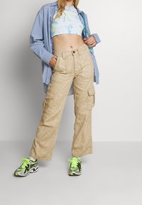Pantalon cargo beige avec un motif tourbillonnant, poches latérales et coupe ample. Associé à un crop top tie-dye et des baskets colorées.
