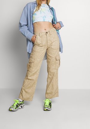Pantalon cargo beige avec un motif tourbillonnant, poches latérales et coupe ample. Associé à un crop top tie-dye et des baskets colorées.