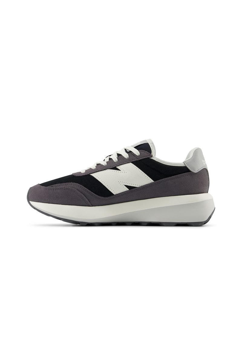 Sportlicher Schuh mit grauem Wildleder und schwarzem Mesh-Obermaterial, ausgestattet mit einem weißen Logo, weißen Schnürsenkeln und einer massiven weißen Sohle. Schwarzes Profildesign.