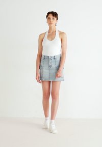 Valge halterneck bodysuit on kombineeritud helesinise teksaseelikuga, millel on taskud ja nööpide sulgemine; mudel kannab valgeid tennisetossusid.