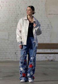 Jacket din piele albă cu broderie în formă de stea, asortat cu blugi blue uzate, echipați cu petice roșii și albe în formă de stea, finalizați cu adidași albi.