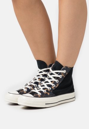 High-top sneakers in black canvas with leopard print accents, white laces, and a rubber toe cap. Features a textured surface and contrasting sole.