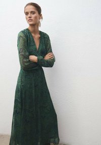 Largo vestido verde con un patrón de cachemira, escote en V profundo y mangas largas de gasa, con una falda fluida que llega a medio pantorrilla.