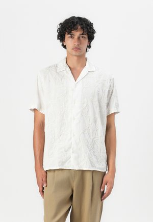 Chemise à manches courtes en tissu blanc avec une broderie florale texturée. Dotée d'un col standard et d'une coupe décontractée. Boutons sur le devant.