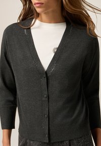 Mörkgrå cardigan med V-ringning, trekvartsärmar och glittrande detaljer längs halslinjen. Har knäppning framtill och en mjuk textur.