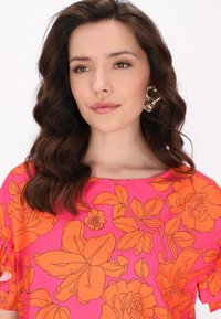 Top roz strălucitor cu un imprimeu floral mare portocalie, mâneci scurte cu volane și un decolteu larg. Designul este neted, cu o textură ușoară.