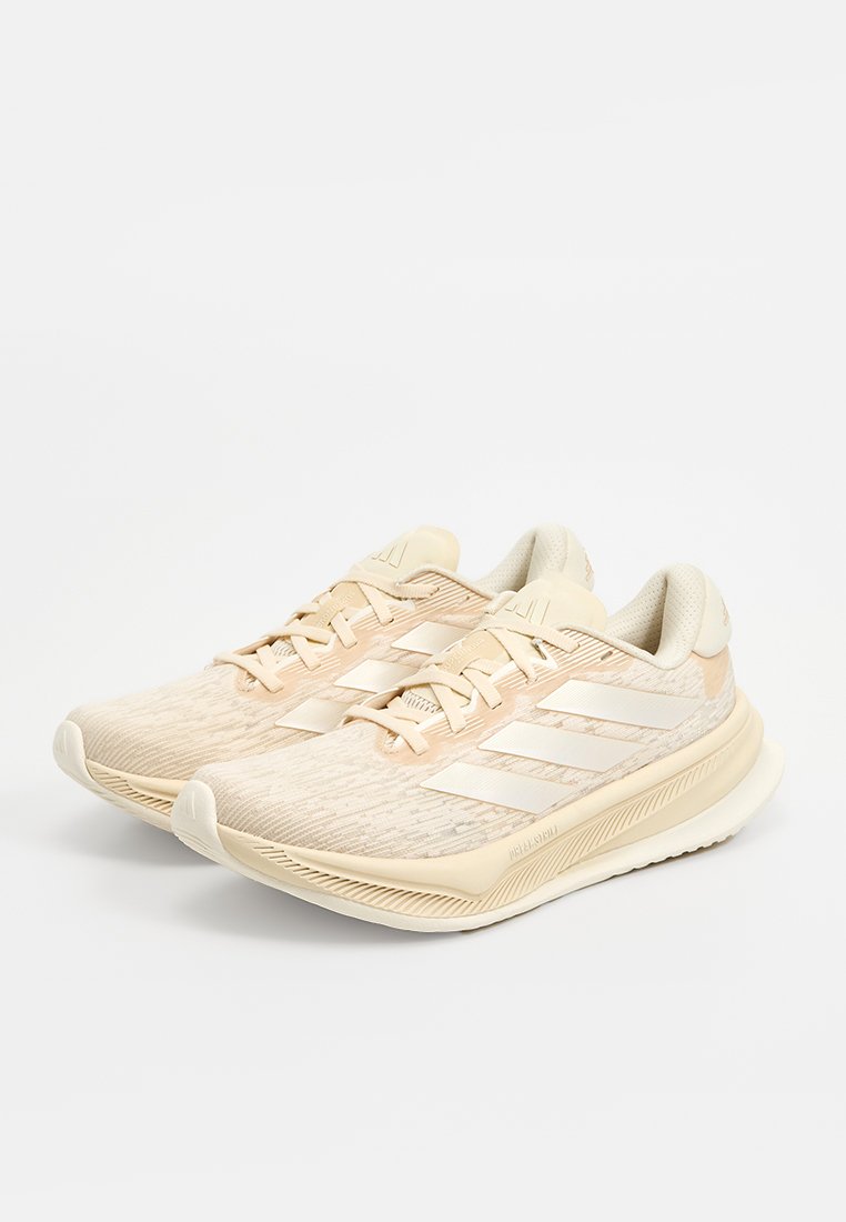 Zapatillas deportivas de color beige claro con una parte superior de malla texturizada, collar acolchado y tres rayas blancas a los lados. Diseño de suela curvada.