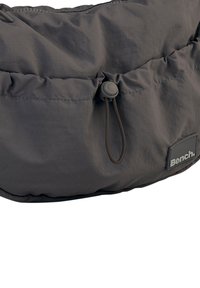 Dunkelgraue, gepolsterte Tasche mitGathered-Oberseite, verstellbarem Kordelzugverschluss und einem strukturierten Etikett mit "Bench." in einem gedämpften Akzent.