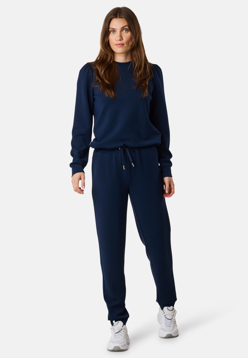 Navy Sweatshirt- und Hosenanzug aus weichem Material, mit Rundhalsausschnitt, elastischem Bund, Kordelzug und gerippten Bündchen. Weiße Sneakers inklusive.