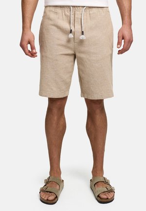 Man draagt beige korte broek met trekkoord en beige sandalen met dubbele bandjes, staand tegen een effen witte achtergrond.