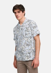 Kortermet blomstret skjorte i lyseblå med svarte og hvite blomstermønstre; avslappet passform; knappekrage; stoffet ser glatt ut.
