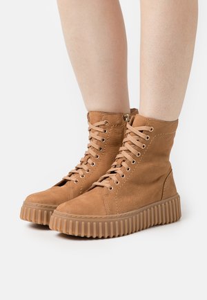 Brown leather high-top sneakers with textured finish, lace-up front, and ridged rubber sole. Side zipper detail for easy wear.
