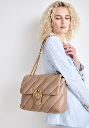 Bolso de mano de piel beige con diseño acolchado, correa de cadena dorada y herrajes decorativos en forma de pájaro. Cierre con solapa, tamaño mediano, superficie suave.