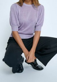 Pull lavande avec manches courtes bouffantes et encolure ronde, associé à un pantalon noir à jambes larges et des mocassins noirs brillants.