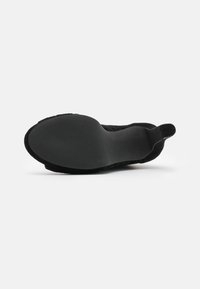 Černé dámské boty na vysokém podpatku zobrazené ze spodu, s hladkou podrážkou a štíhlým podpatkem na bílém pozadí.