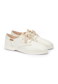 Zapatos de cuero blanco con cordones y plantillas en beige. Diseño de punta redonda, textura suave, con una etiqueta de marca en tono marrón en el costado y una suela flexible.
