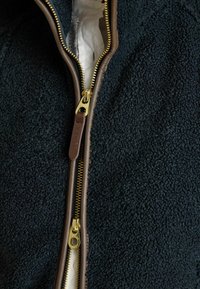 Dunkelblaues Fleece-Jackett mit einem braunen Reißverschluss. Goldener Metall-Reißverschlusszug und sichtbare Stoffinnenverkleidung. Strukturiert Oberfläche verbessert die Wärme.