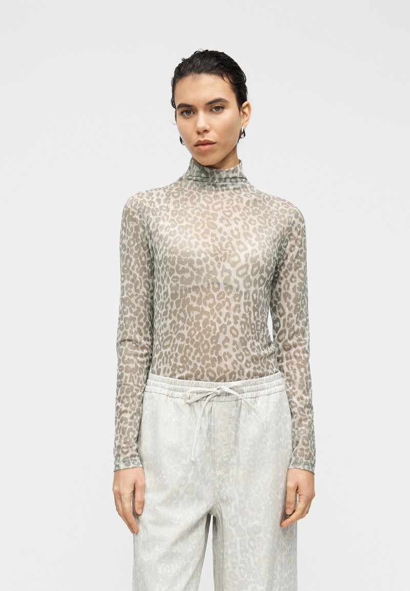 Διαφανές τοπ με μακριά μανίκια σε ανοιχτό γκρι χρώμα με λεοπάρ μοτίβο, ψηλό γιακά και εφαρμοστή γραμμή, συνδυασμένο με ανοιχτόχρωμο παντελόνι με διακριτικό σχέδιο.