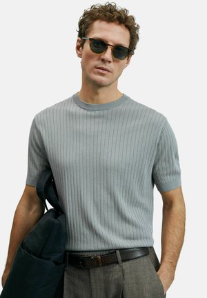 Helles graues, geripptes Kurzarm-Pullover mit Rundhalsausschnitt, kombiniert mit einem dunklen Gürtel und einer schwarzen Tasche. Glatte Textur, taillierte Passform.