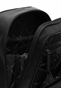 Musta nahkareppu, jonka sisällä on useita vetoketjullisia taskuja, tekstuurilla varustettu kangaspäällyste, joka esittelee brändin logon. Sujuva ja kestävä viimeistely.