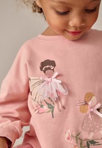 Sweatshirt roz cu un grafic cu dansatori de balet, cu accente din tul și fundițe. Fabricat dintr-un material moale, are manșete cu țesătură rigată și o croială lejeră.