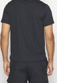 Czarna krótka koszulka z rękawem, wykonana z gładkiego materiału, z okrągłym dekoltem i prostym wykończeniem, pokazana z tyłu z widocznymi szwami bocznymi.