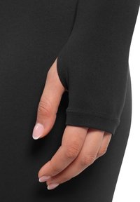 Langärmliges schwarzes Kleidungsstück mit Daumenlöchern, glatter Textur, nahtlosem Design und taillierter Silhouette. Hand mit manikürten Nägeln hält den Ärmel.
