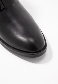 Scarpa in pelle nera con punta affusolata, accenti testurizzati e bordatura cucita lungo la suola, caratterizzata da una finitura liscia.
