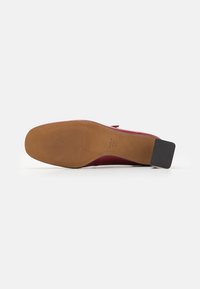 Red leather shoe sole with a smooth finish, featuring a brown base, textured grip, and a rectangular black heel accent.