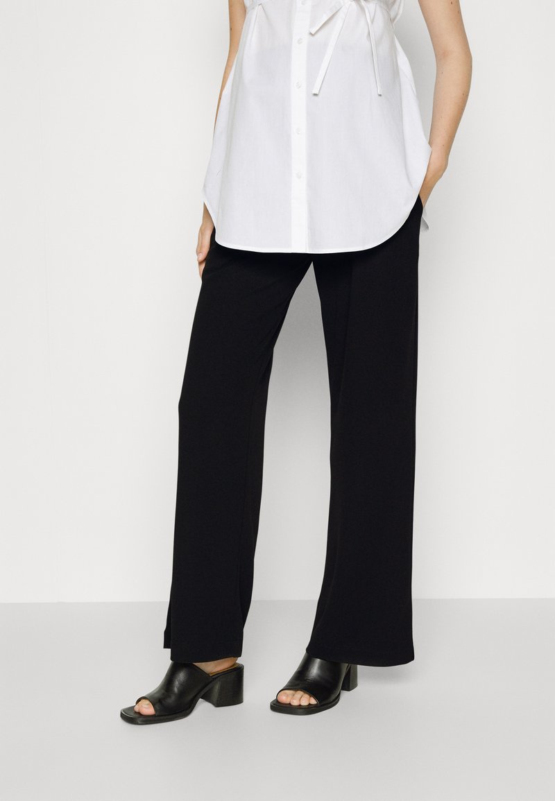 Black wide-leg pants made of lightweight fabric, paired with a white shirt. Black heeled sandals with an open toe complete the outfit.
