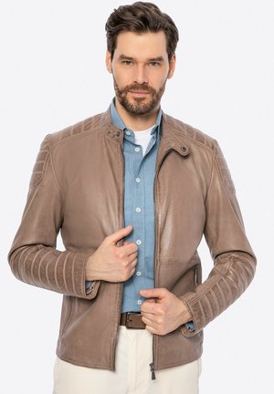 Giubbotto in pelle marrone con accenti a coste sulle spalle e chiusura con zip. Indossato sopra una camicia azzurro chiaro, caratterizzata da una texture liscia e una vestibilità su misura.
