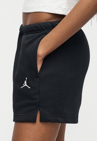 Κοντινό πλάνο ενός ατόμου που φοράει μαύρο αθλητικό σορτς με μικρό λευκό λογότυπο Jumpman, το χέρι τοποθετημένο μέσα στην πλαϊνή τσέπη.